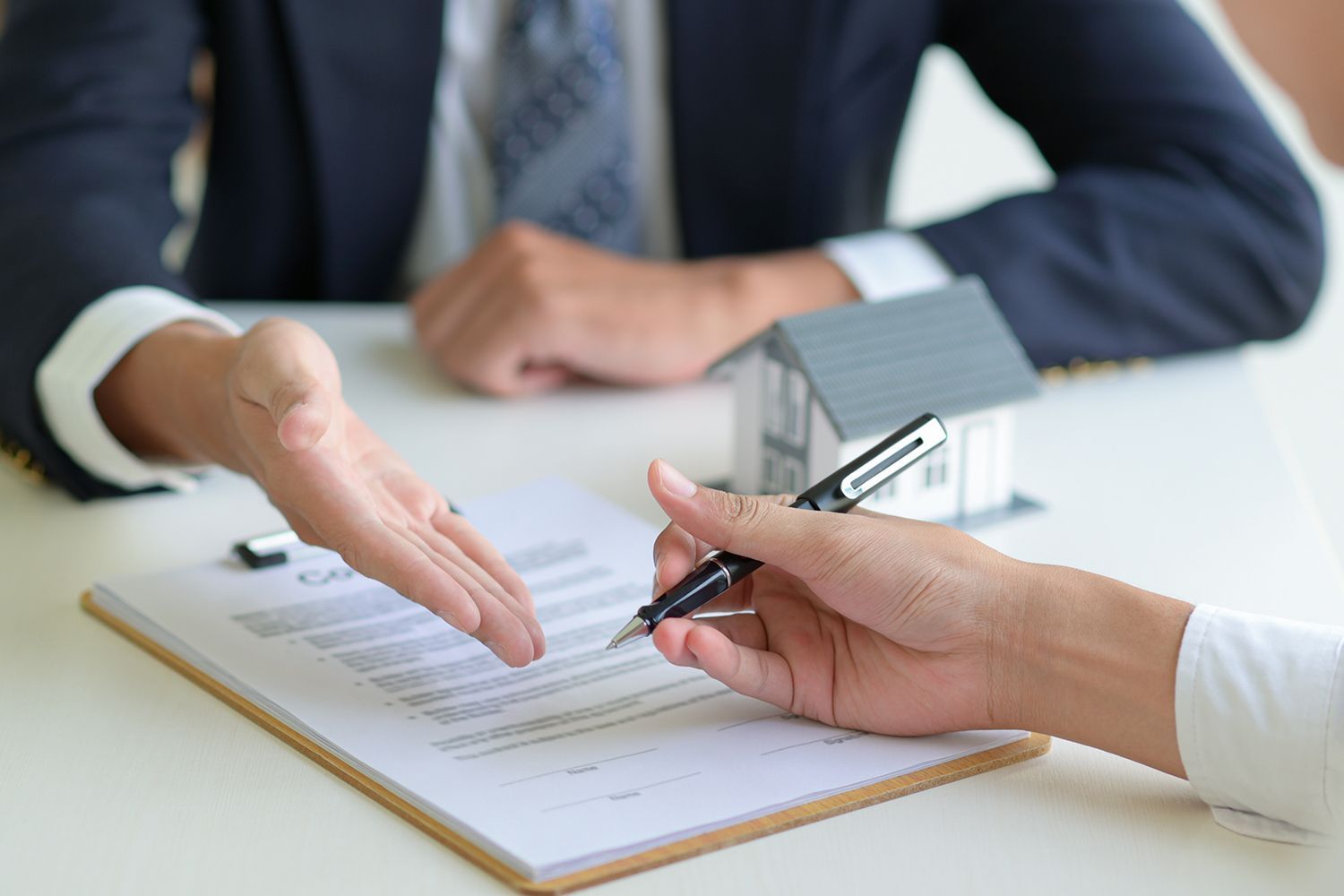 Person handing over keys after signing a document, next to a model house.