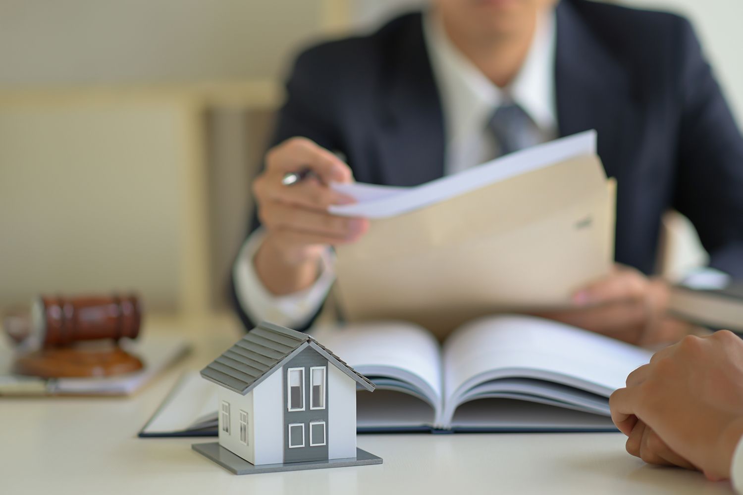Real estate agent presenting documents near a small house model and open book.