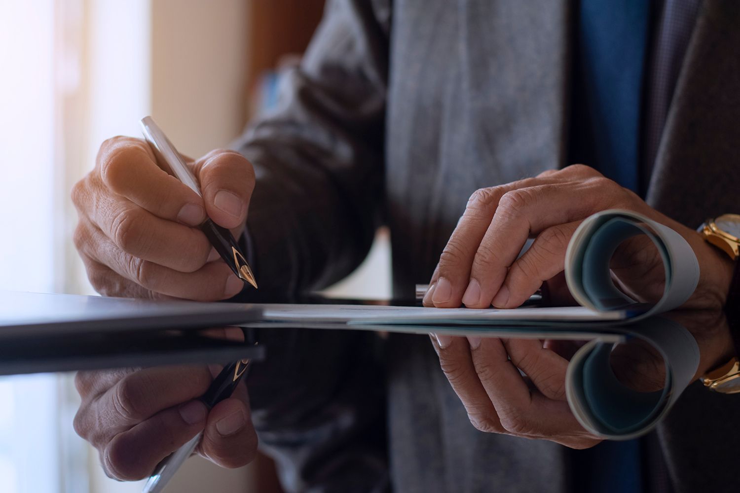 Person signing a document with a pen, close-up. Table with reflections, watch on wrist.