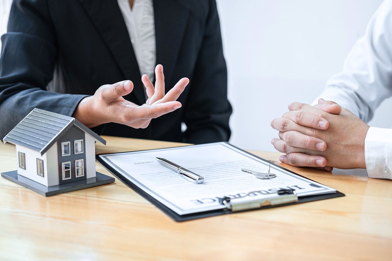 Real estate agent gesturing toward a document with a miniature house and client; office setting.