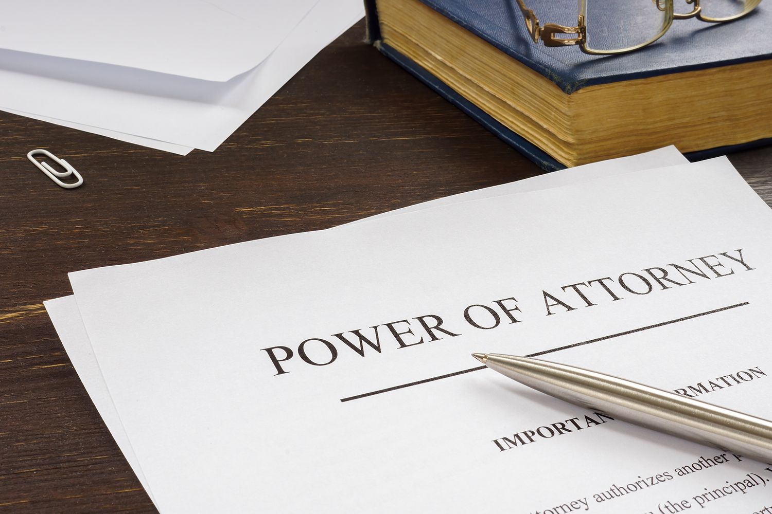 Power of Attorney document with a pen, book, glasses, and paperclip on a wooden desk.