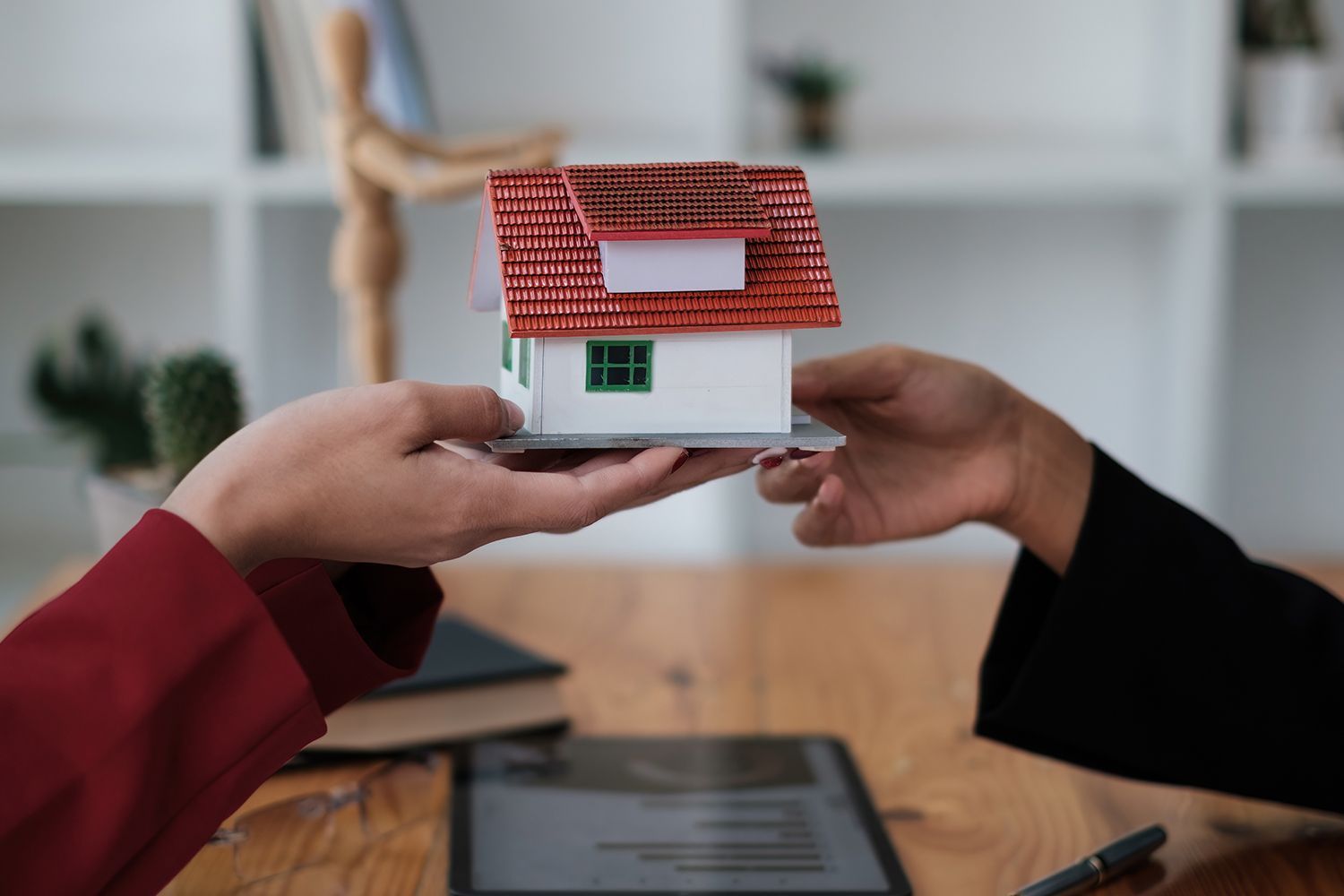 Two people holding a miniature house, possibly a real estate transaction, indoors.