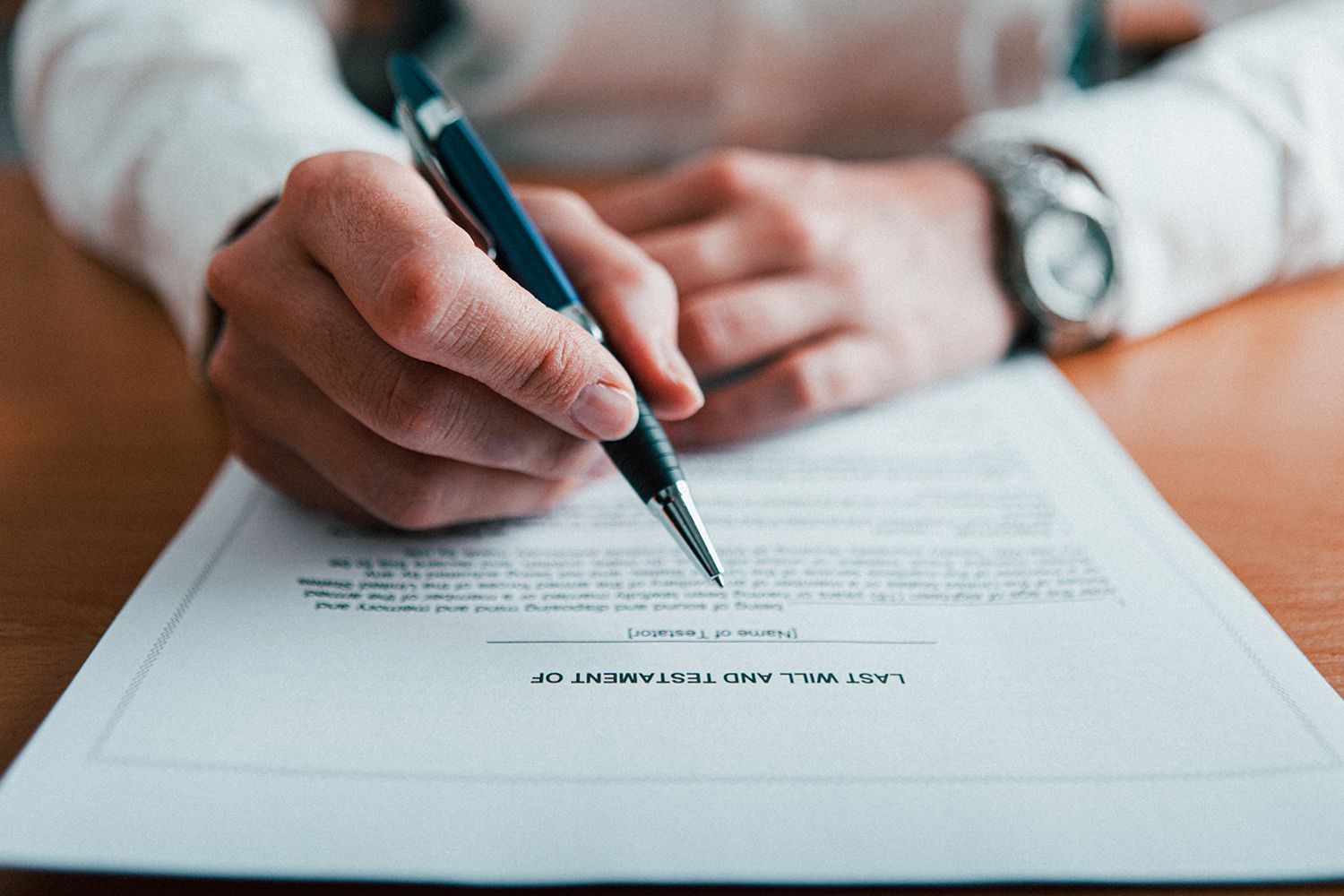 Person signing a document with a pen, close up of hands and watch.