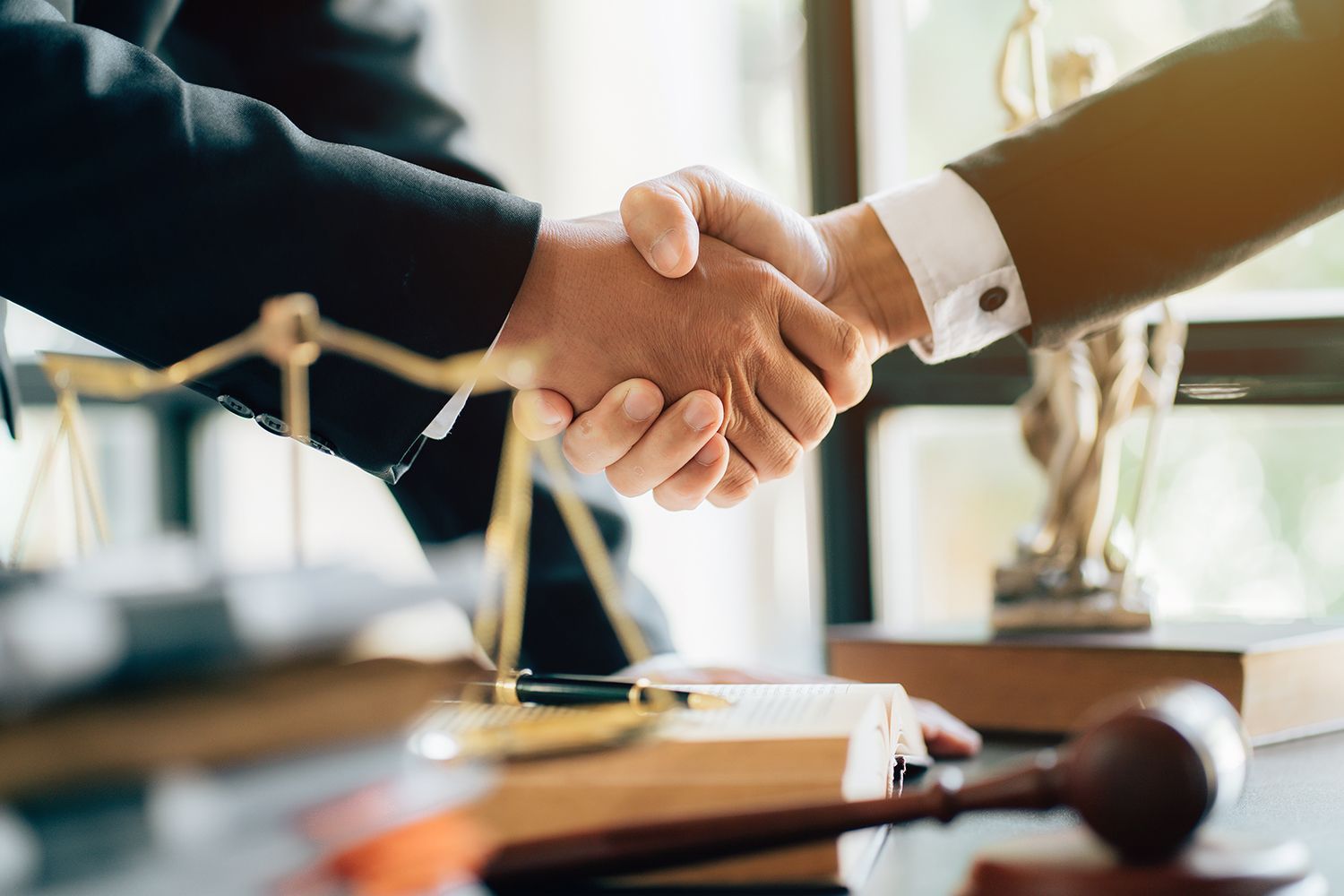 Two people shaking hands near legal symbols, suggesting a deal or agreement. Two people shaking hands near legal symbols, suggesting a deal or agreement.