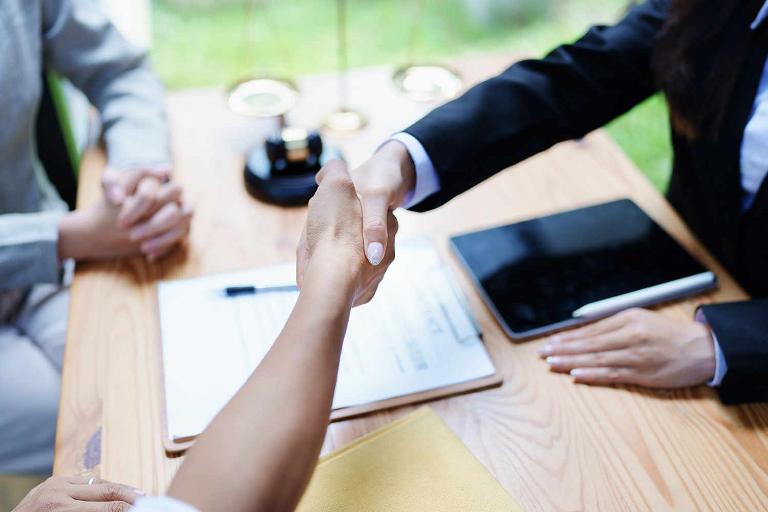 Two people shaking hands over a desk with documents and a tablet.
