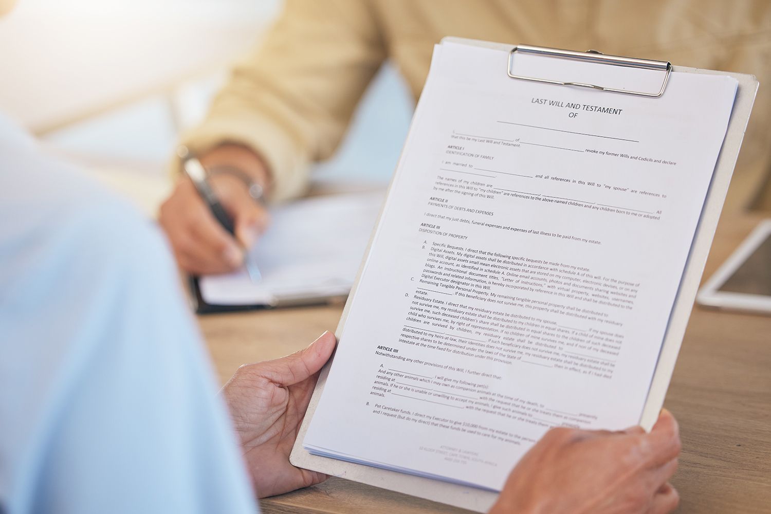 Person holding a clipboard with document while another person writes; office setting.