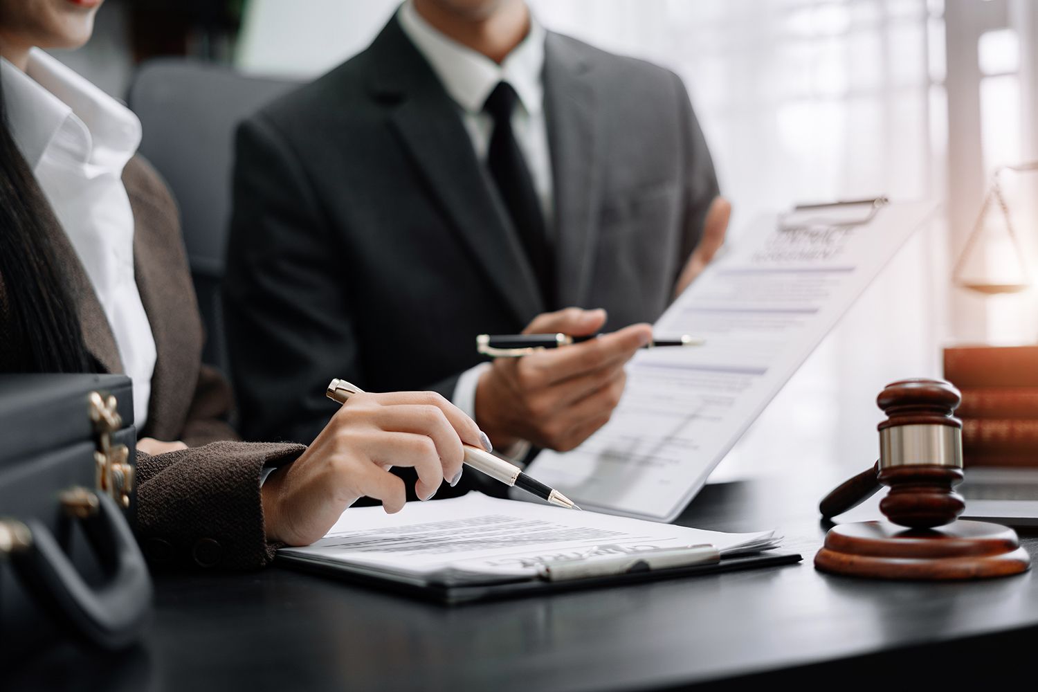 Two lawyers reviewing documents; one points, the other writes. Gavel and law books visible.