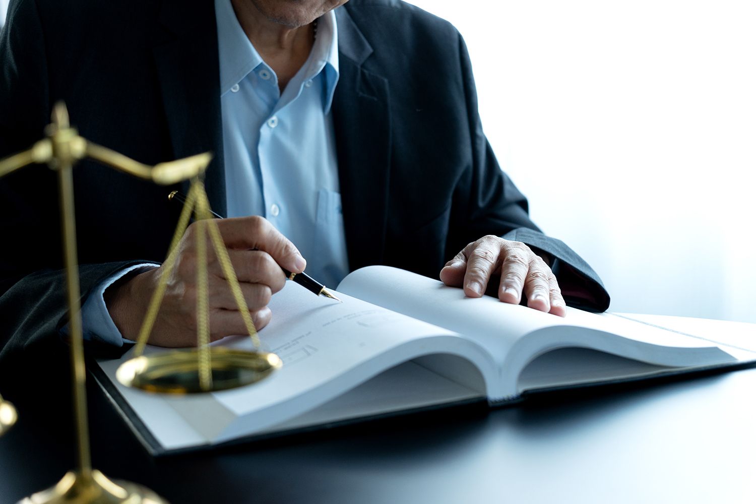 Person in a suit writing in a book, next to a golden balance scale.