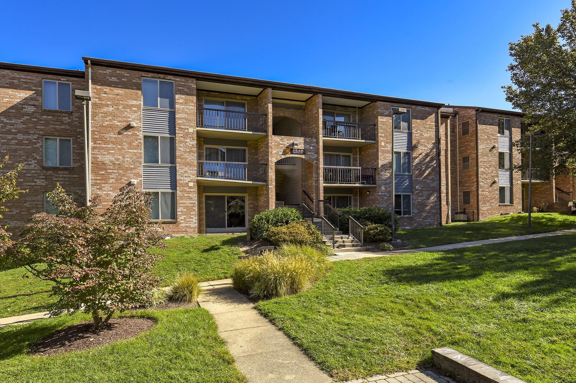 Brick apartment building exterior with balconies and manicured landscaping.