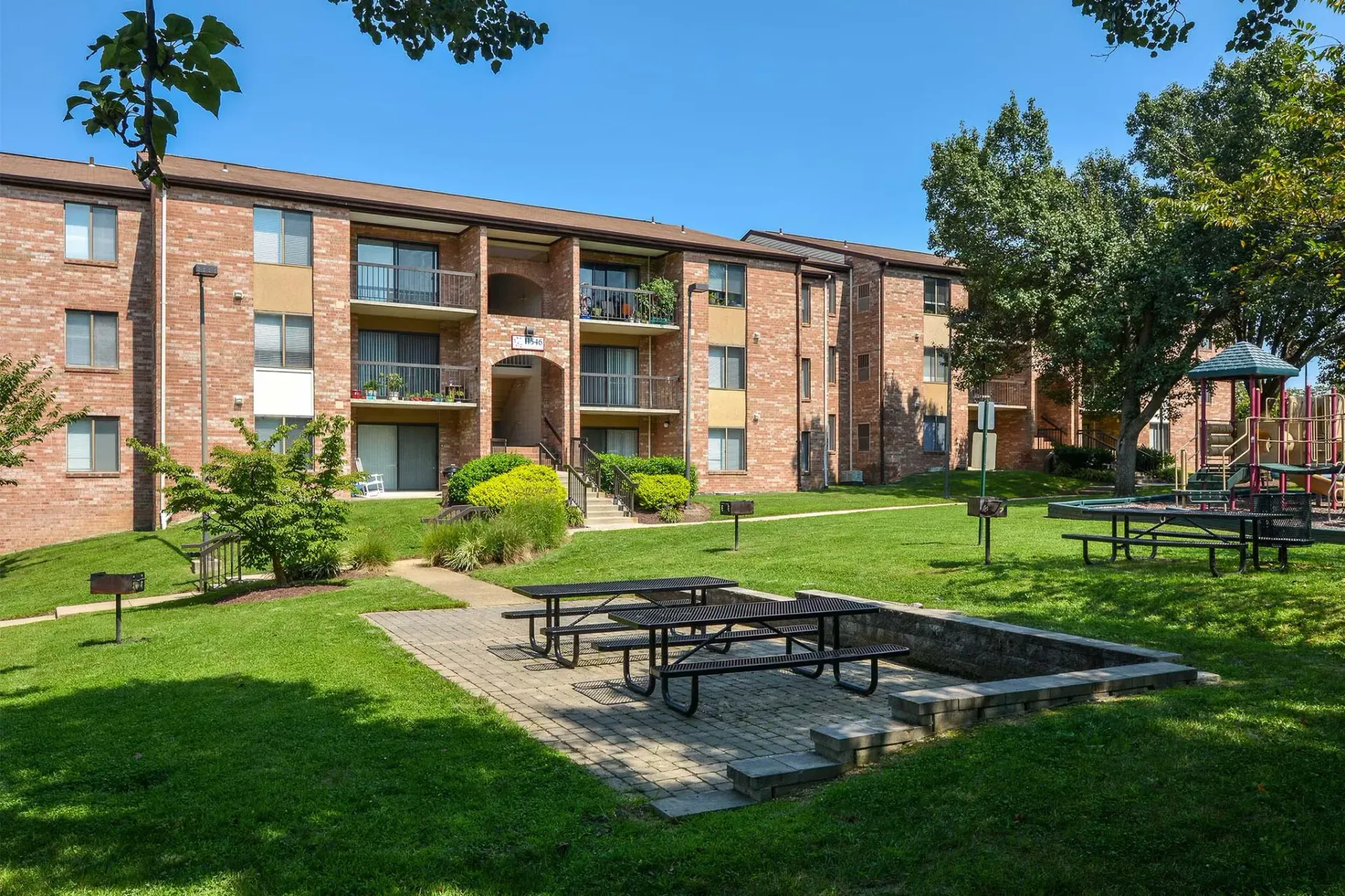 Apartment building with brick facade, green lawn, picnic tables, and a fire pit area.