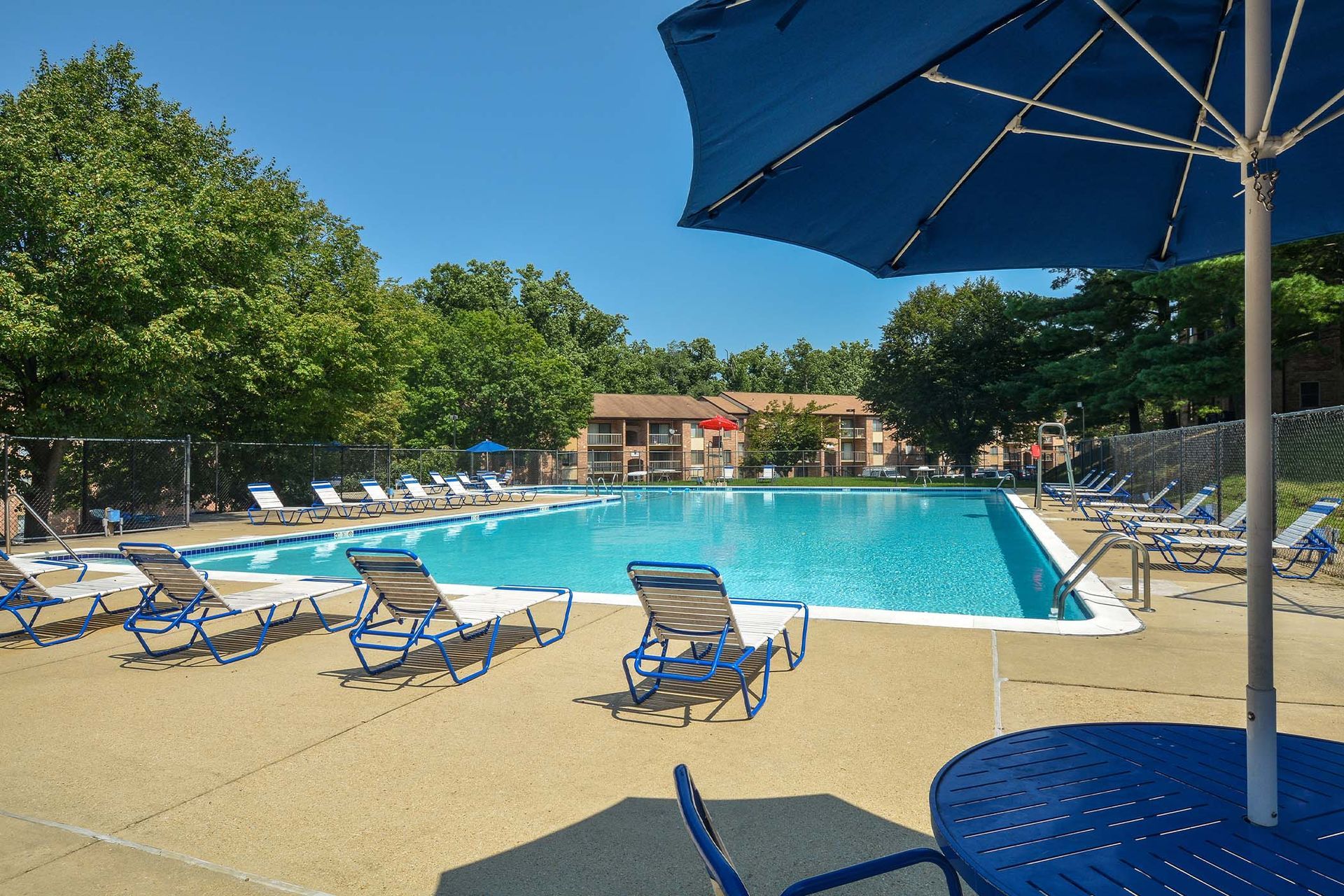 Outdoor community pool area with blue lounge chairs and a large umbrella.
