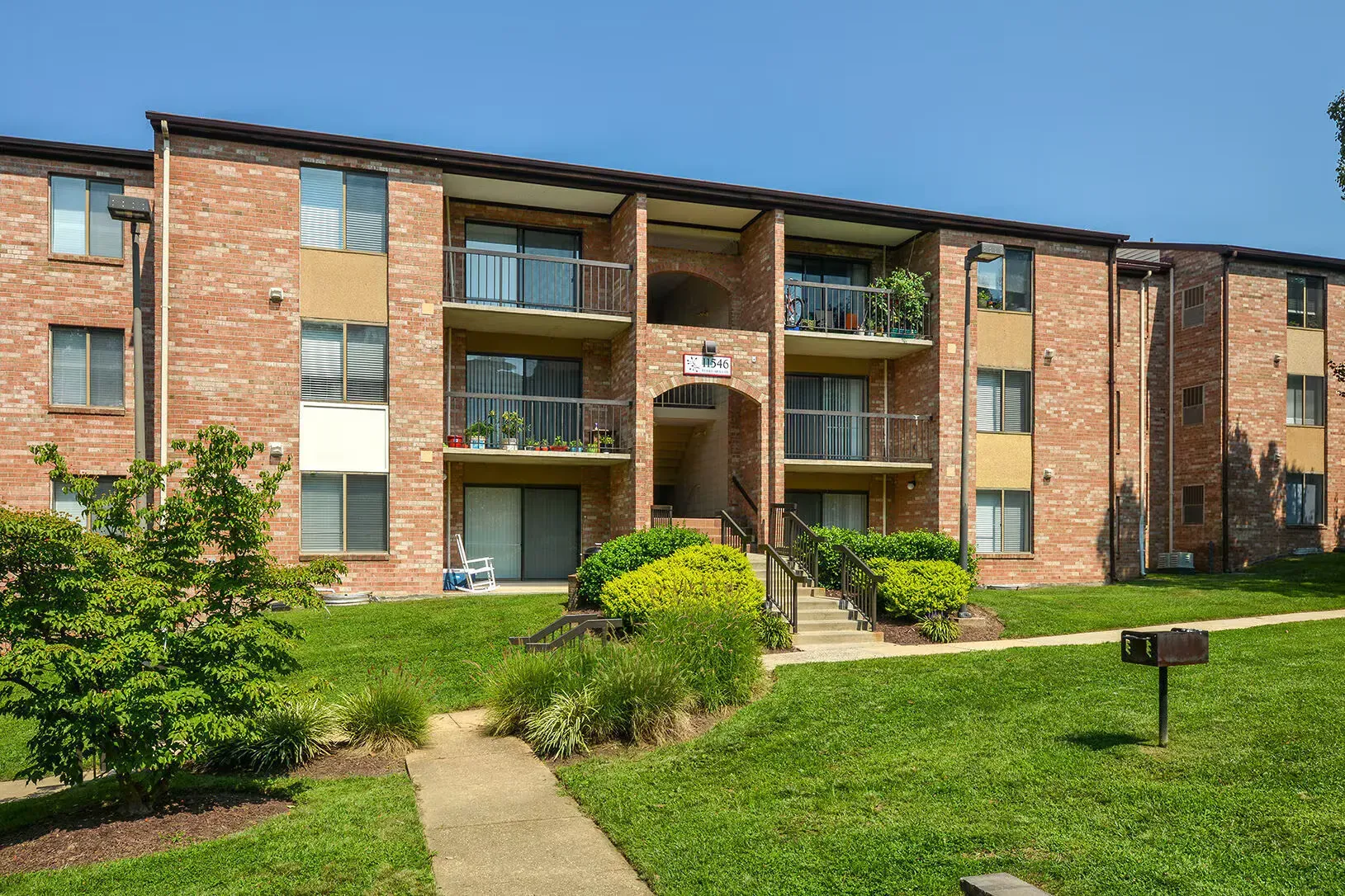 Exterior brick apartment building with balconies and a landscaped lawn.
