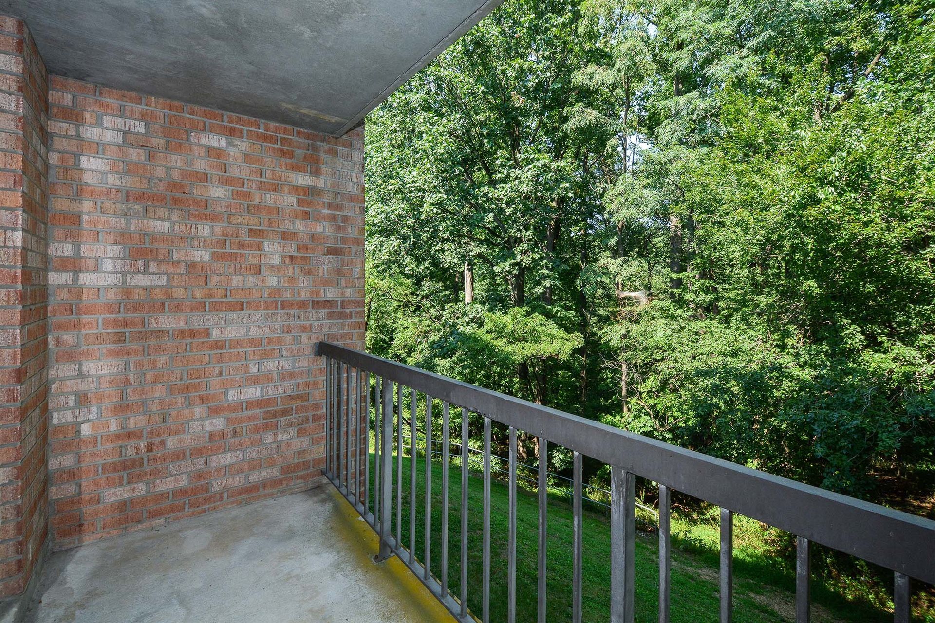 Balcony with brick wall and metal railing overlooking lush trees.