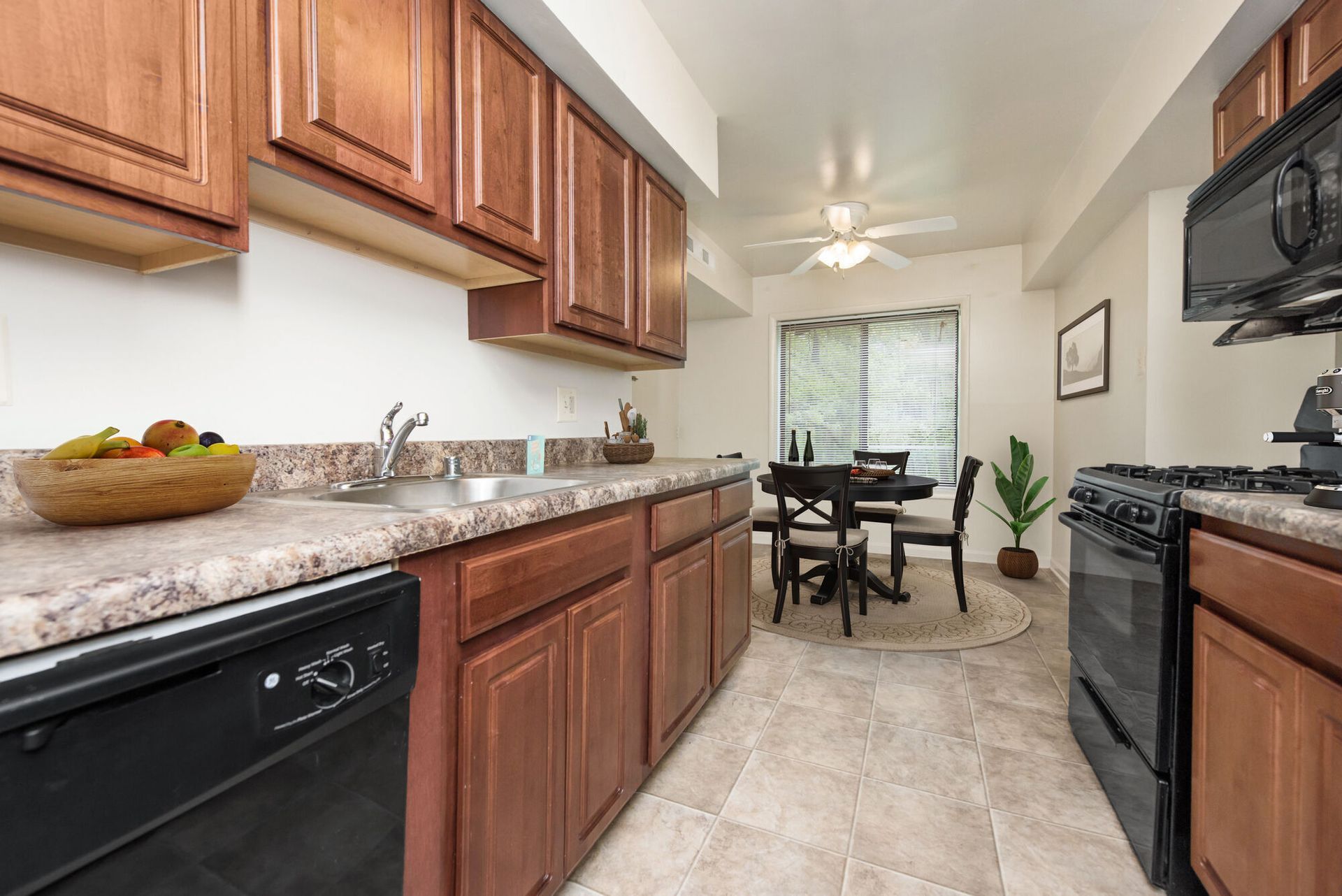 Kitchen with dark wood cabinets, speckled beige countertops, a double sink, and a dining area by a window.