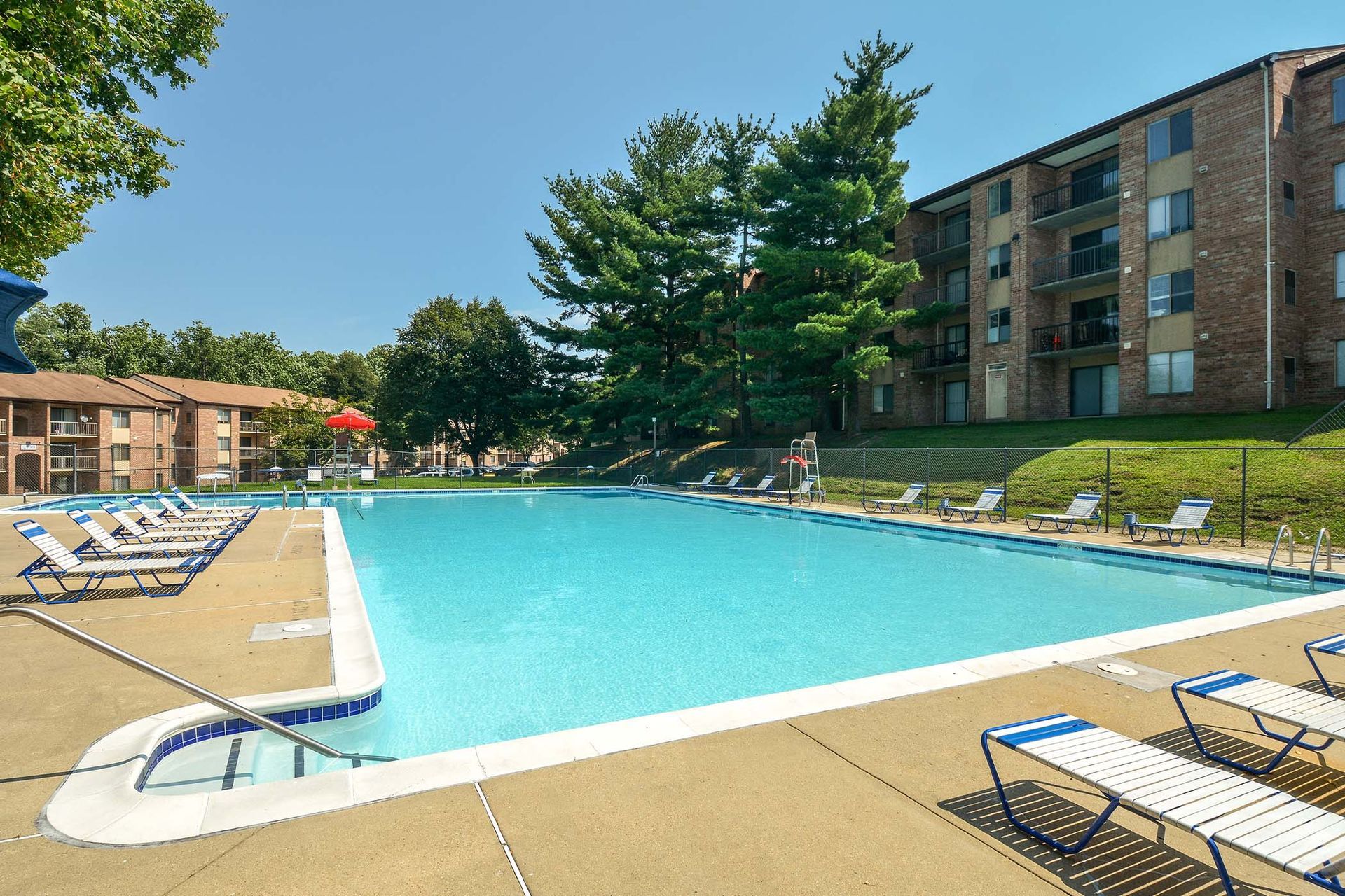 Outdoor pool at apartment complex with lounge chairs and brick buildings in the background.