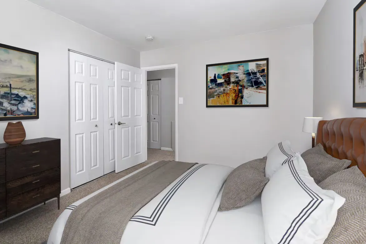 Bedroom in an apartment with a made bed, dresser, and framed art on light gray walls.