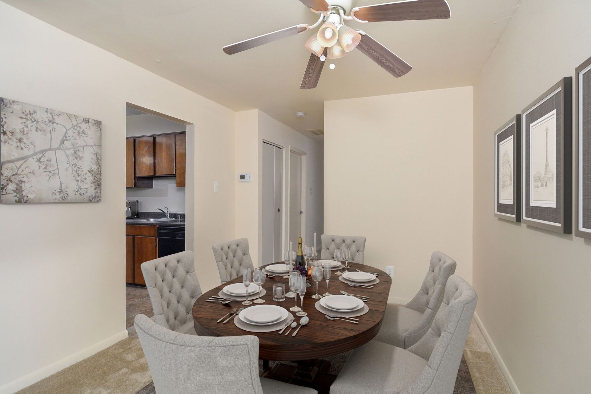 Dining room with a round wooden table and eight beige upholstered chairs beneath a ceiling fan.