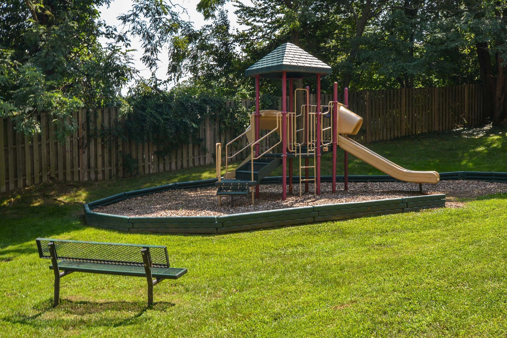 Playground set with slide and climbing structures in a grassy yard, fenced by wood.