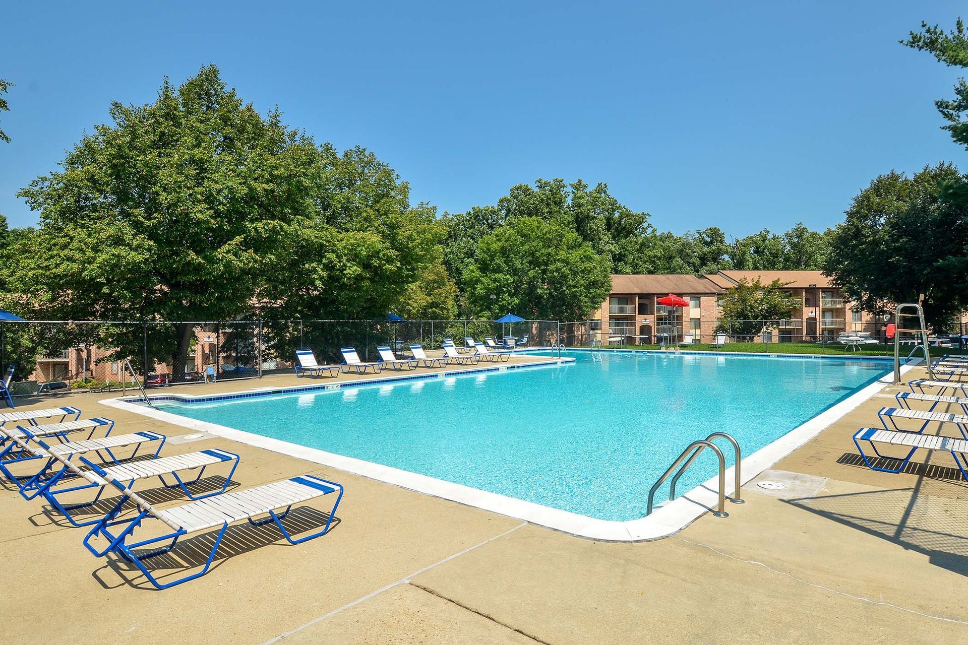 Outdoor community swimming pool with blue water, surrounding lounge chairs, and trees.