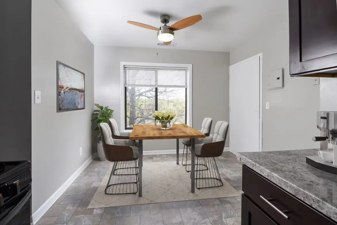 Dining area in an apartment with a wooden table, six chairs, a ceiling fan, and a large window.
