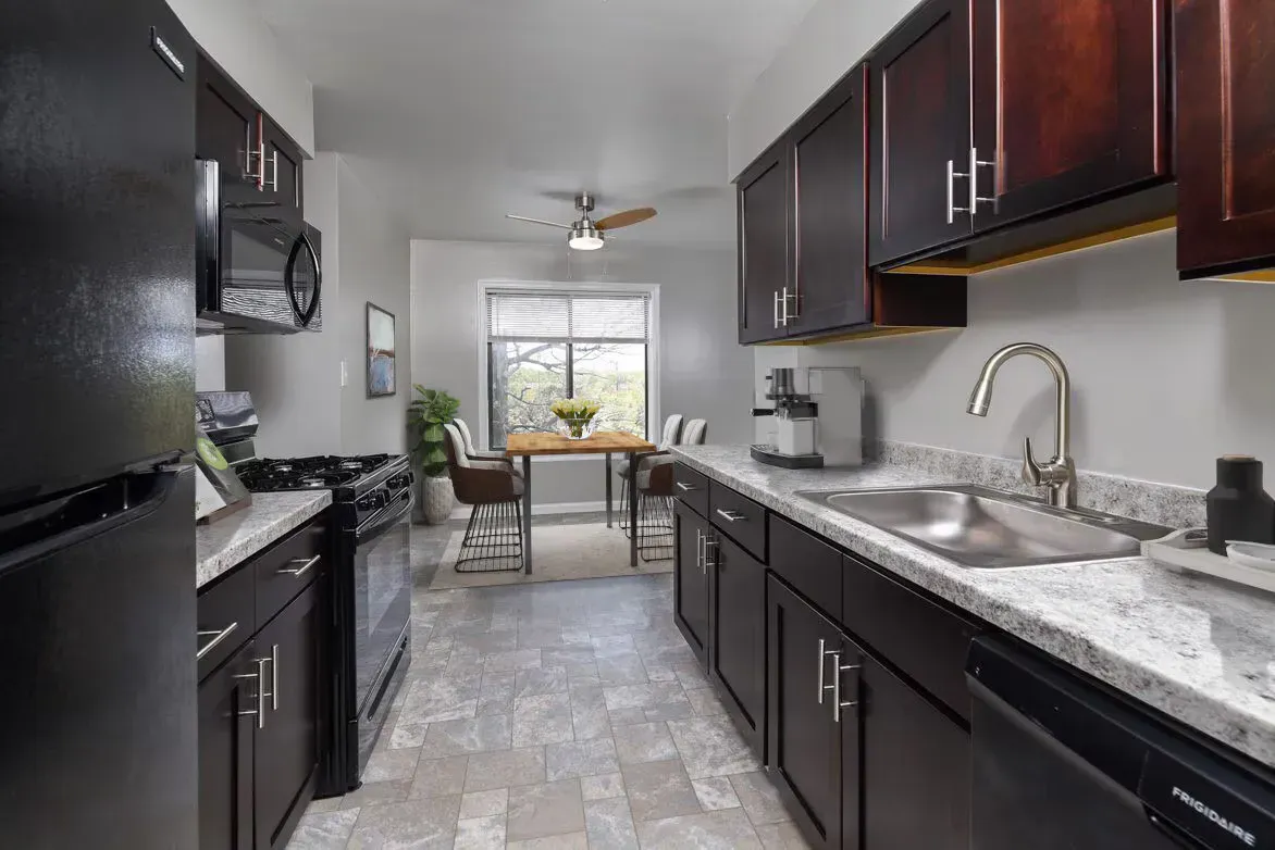 Modern galley kitchen in an apartment with dark cabinetry, granite countertops, and stainless appliances.