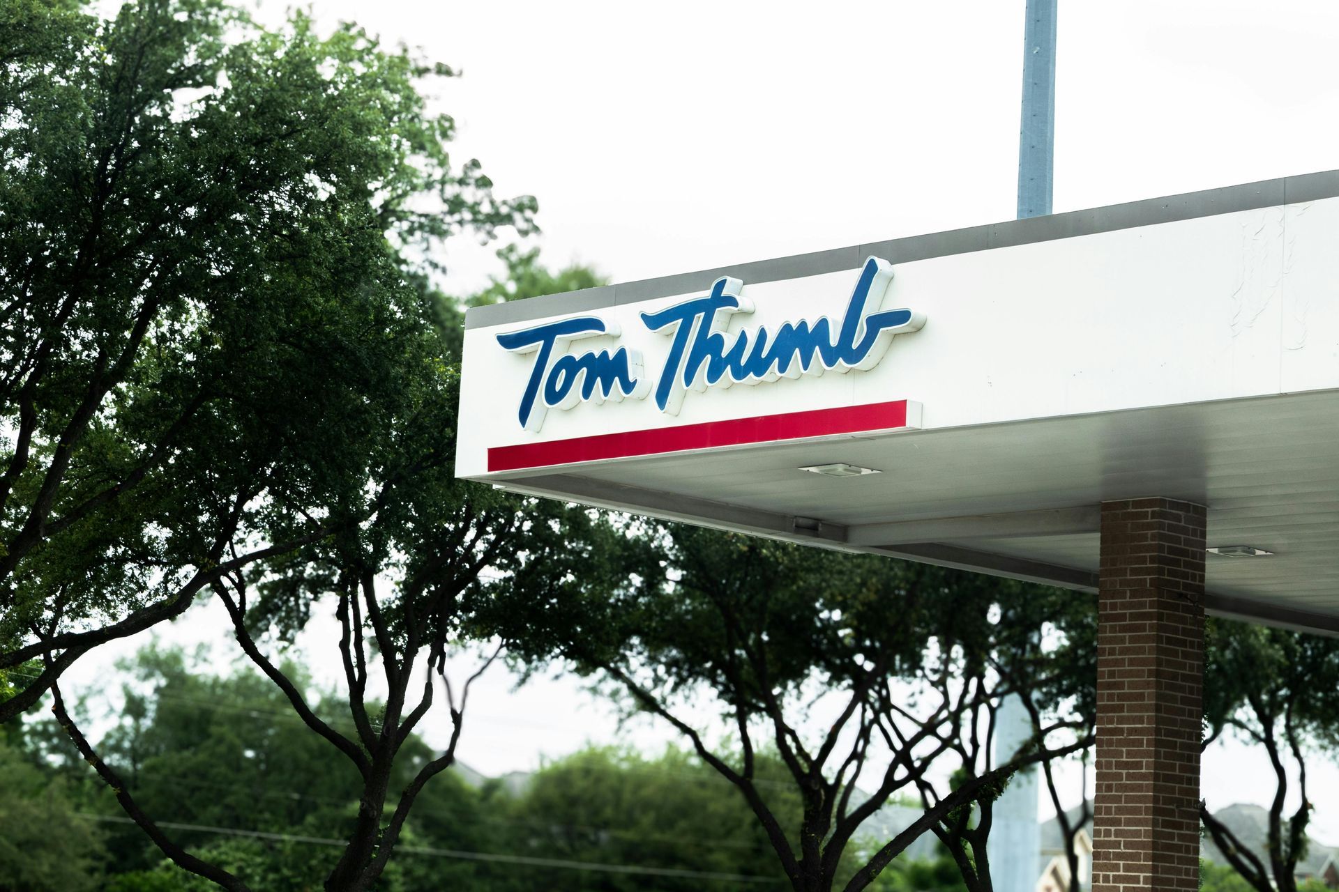 Tom Thumb gas station sign with blue lettering over a red stripe, trees in the background.