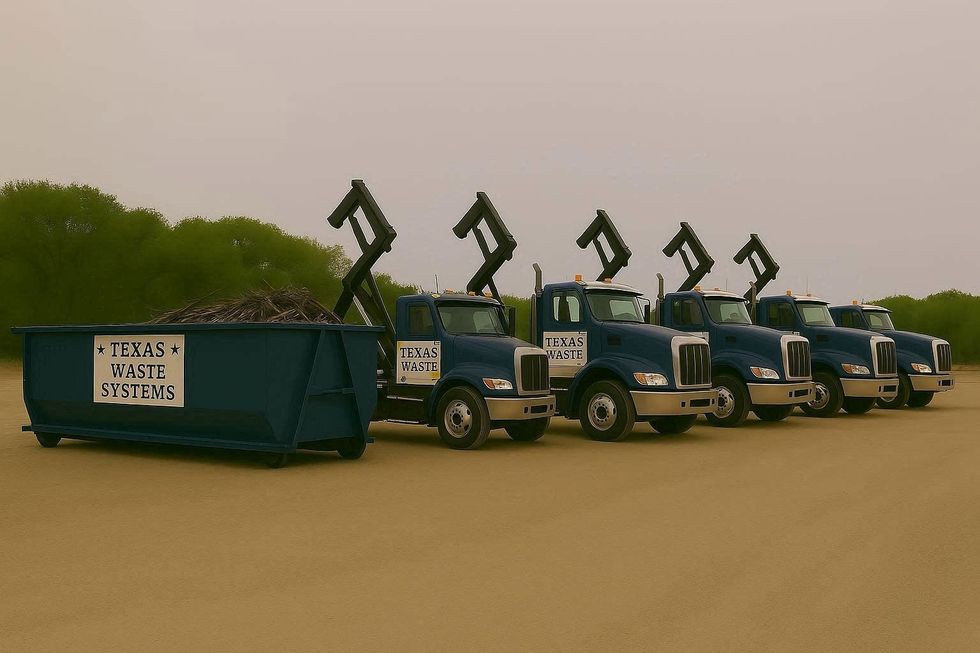 Line of blue roll-off trucks with raised arms and a full dumpster in a field.