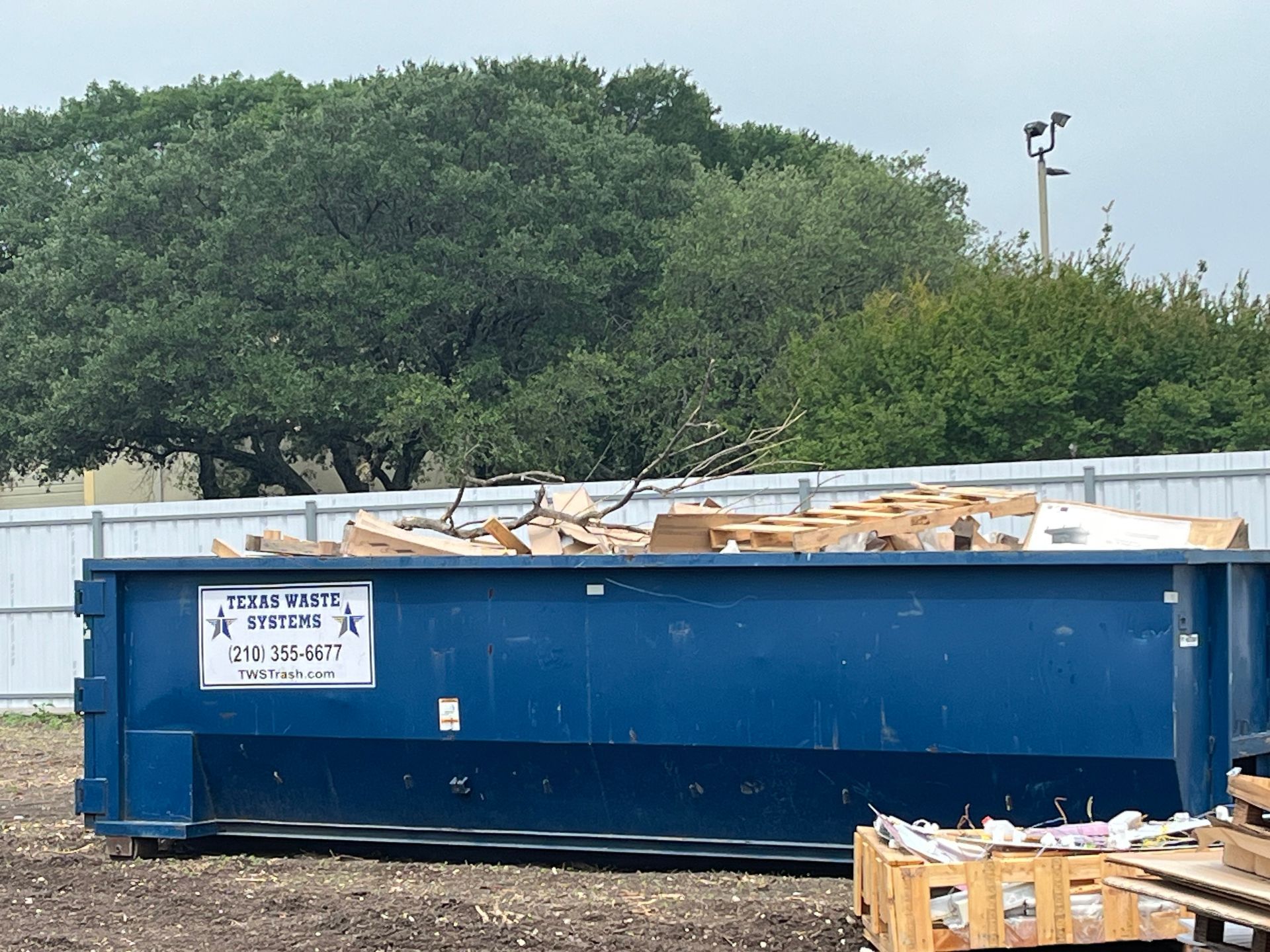 Blue dumpster filled with wooden materials in an outdoor setting.
