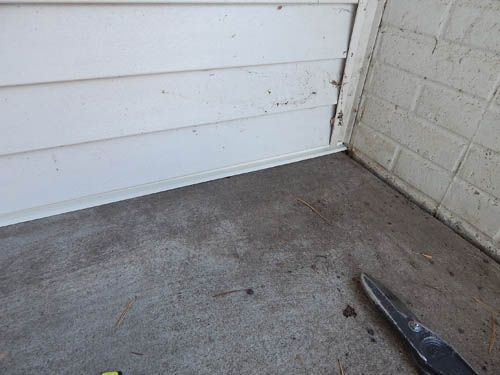 White siding meets a brick wall on a concrete surface