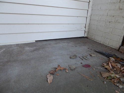 Concrete porch next to white siding and a brick wall with scattered leaves