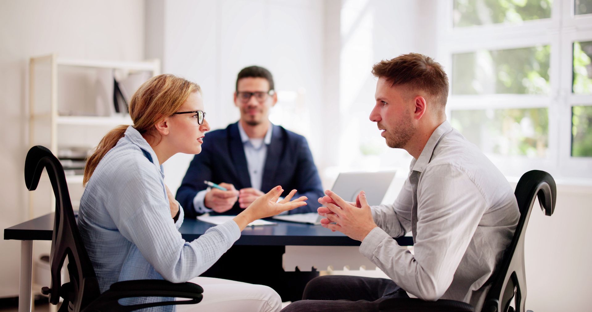 Woman and man in a heated discussion, with a mediator in the background in an office. Woman and man in a heated discussion, with a mediator in the background in an office.