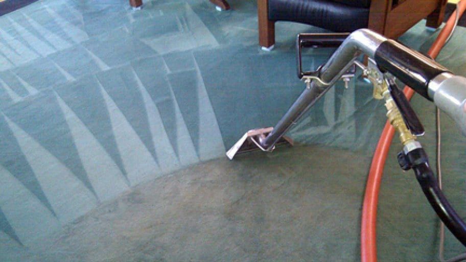 A vacuum cleaner is cleaning a green carpet in a living room.