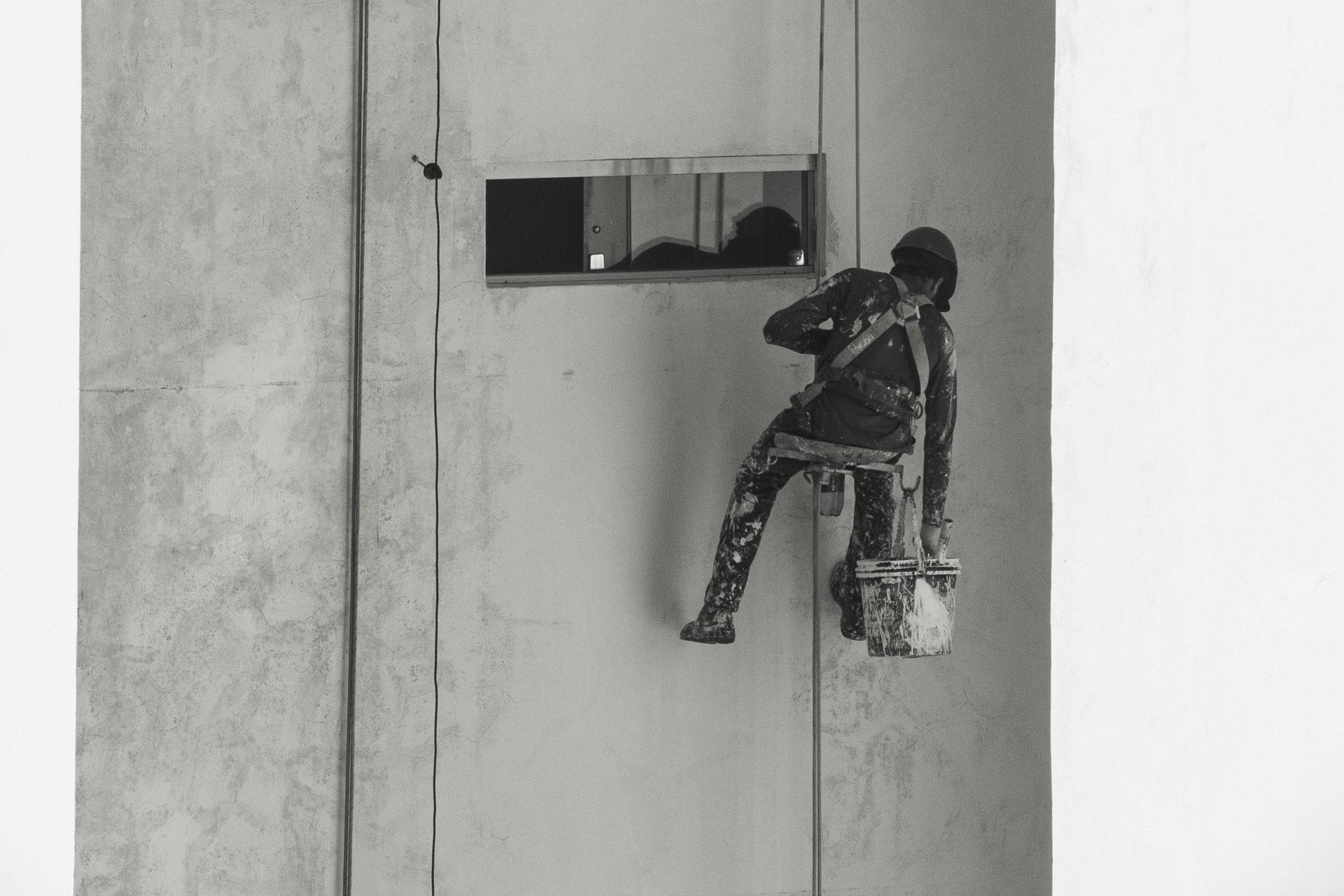 A black and white photo of a man painting a wall.