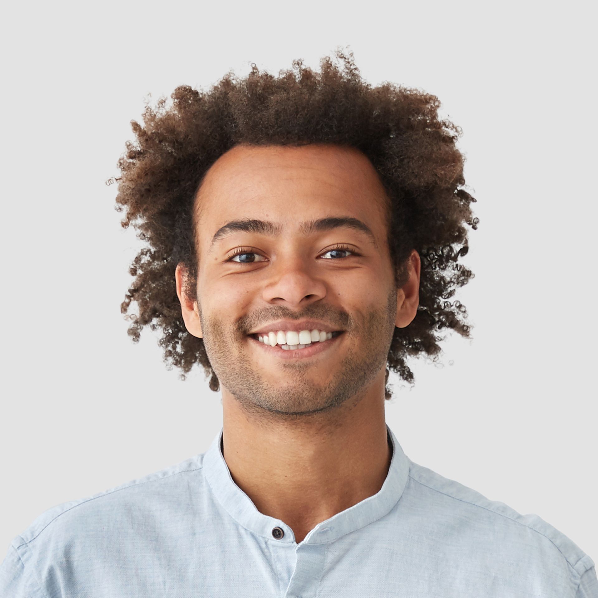 A man with curly hair is smiling and wearing a blue shirt.