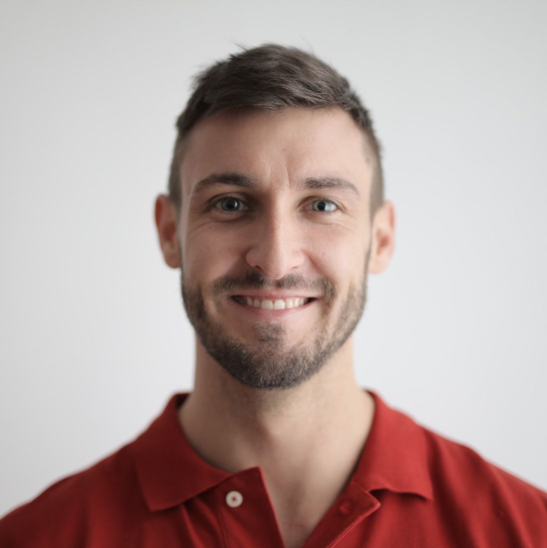 A man with a beard is wearing a red polo shirt and smiling.