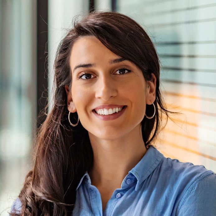 A woman wearing a blue shirt and hoop earrings is smiling for the camera.