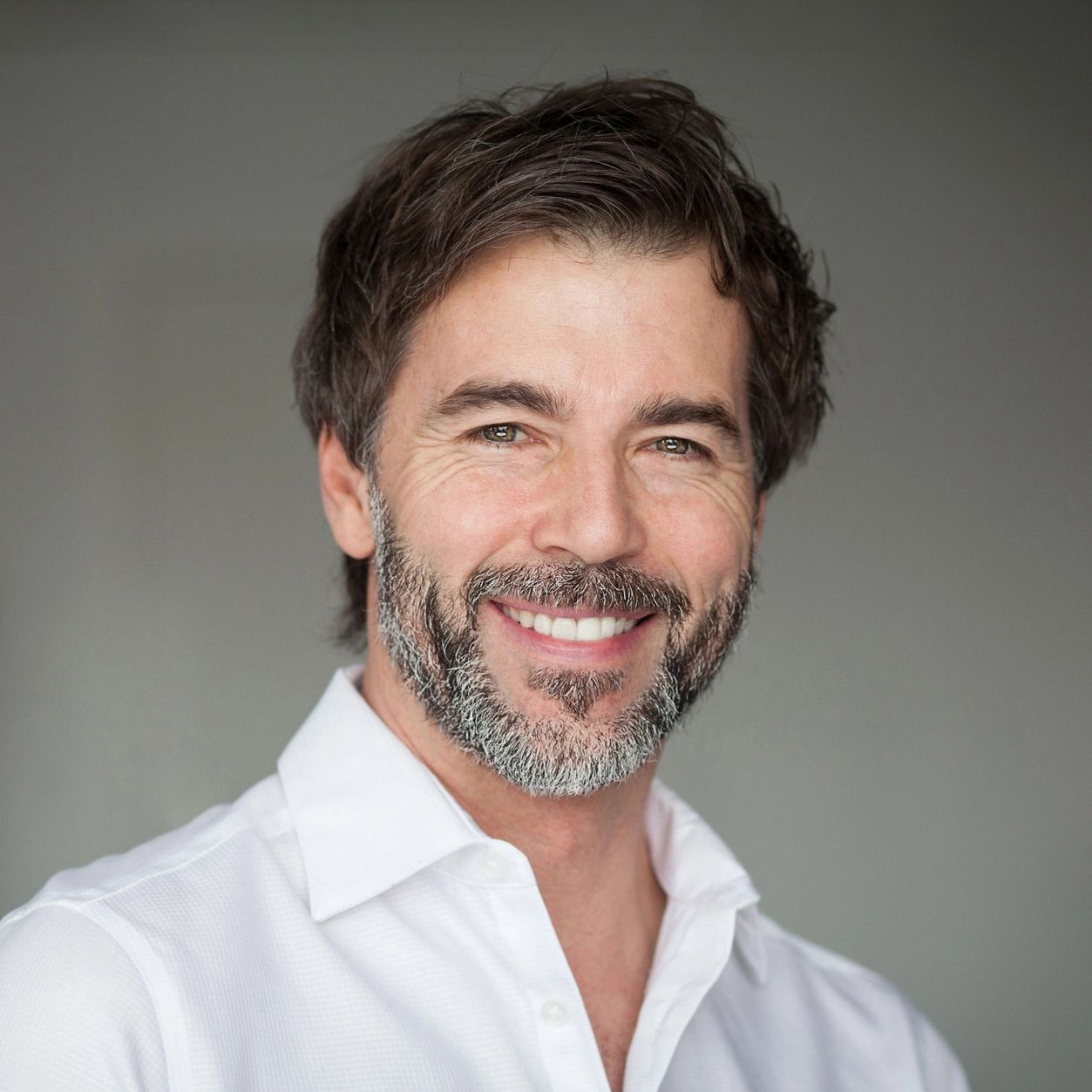 A man with a beard and a white shirt is smiling for the camera.