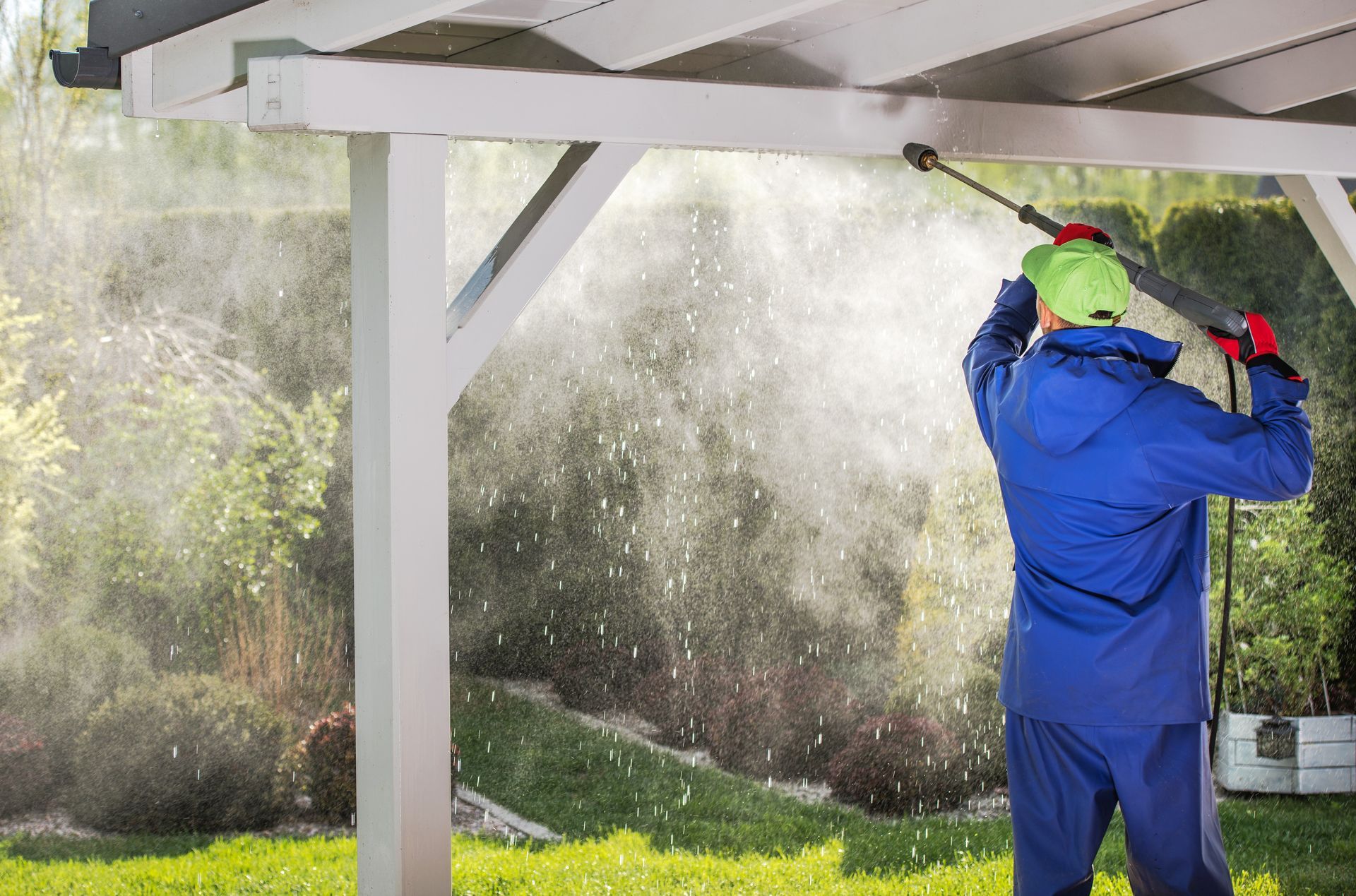 A man is using a high pressure washer to clean a carport.