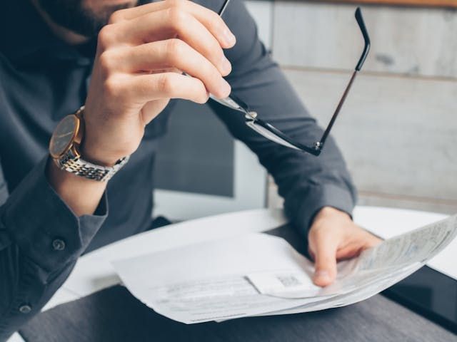 Person holding glasses in one hand and papers in the other hand