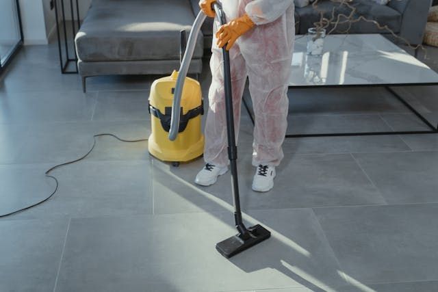 Person wearing gloves and a Tyvek suit using an industrial vacuum