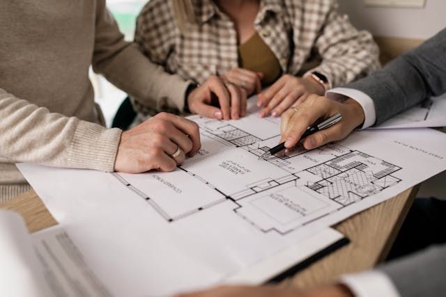 Three people with their hands on a blueprint of a home