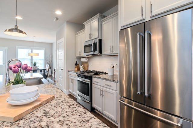 a kitchen with granite counters, white cabinets and stainless steel appliances