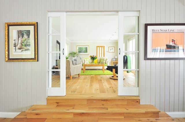 a living room with white sliding doors, light wood flooring and green decor