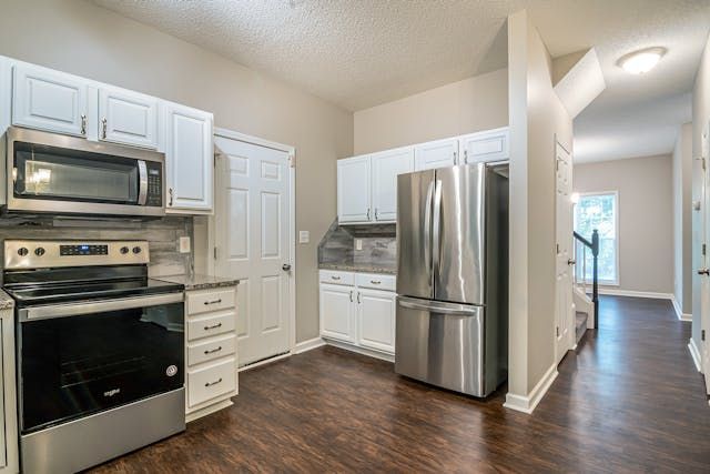 a white kitchen with hardwood flooring and stainless steel appliances