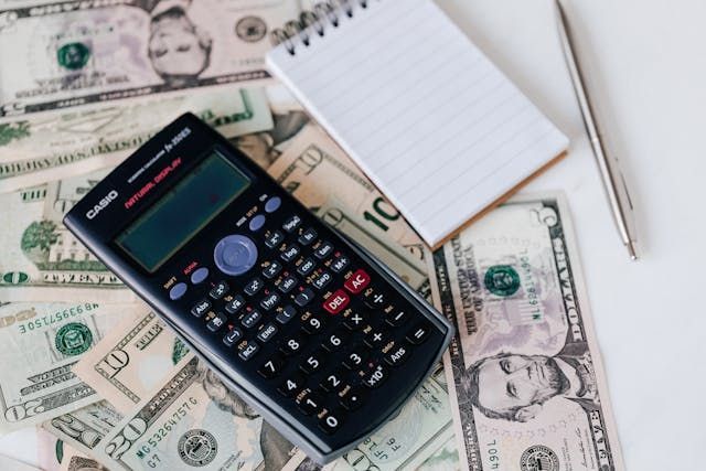 calculator and note pad on top of dollar bills