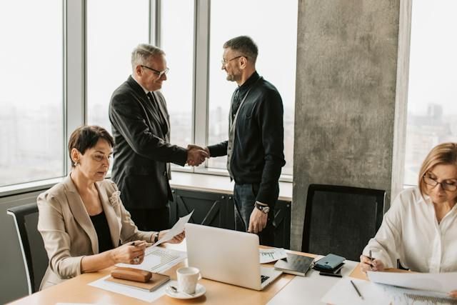four people in a conference room as two people shake hands
