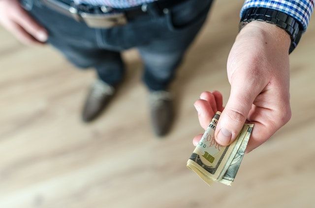 person handing over several one hundred dollar bills