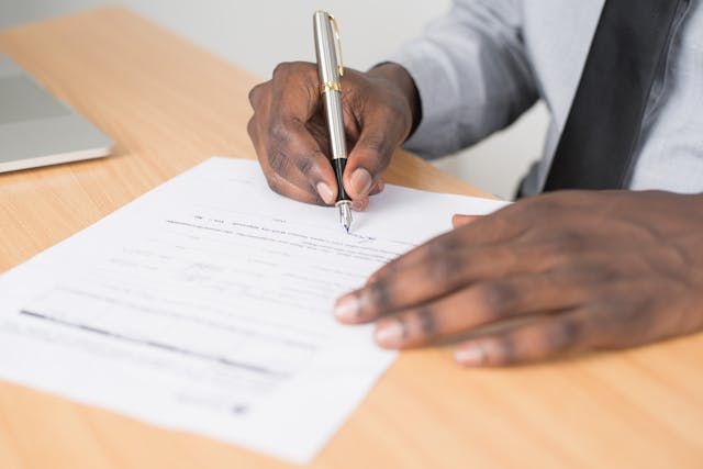 person signing a document with a silver pen