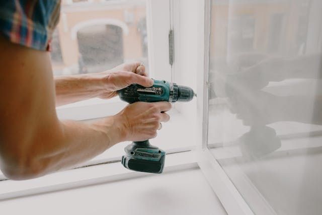 person using an electric drill to fix a window hinge