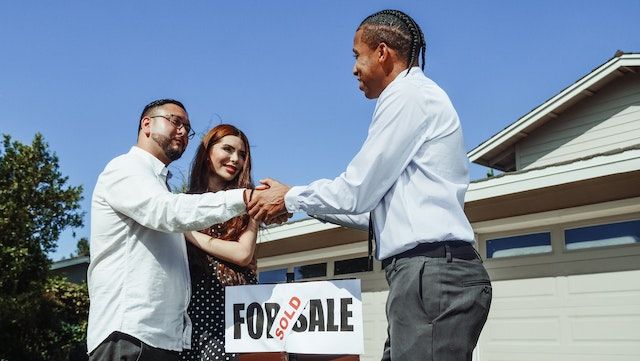 three people shaking hands in front of a sold house